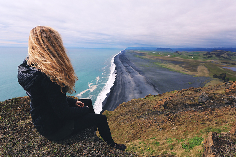 woman sitting alone on a hill looking at the beach is it weird to travel solo