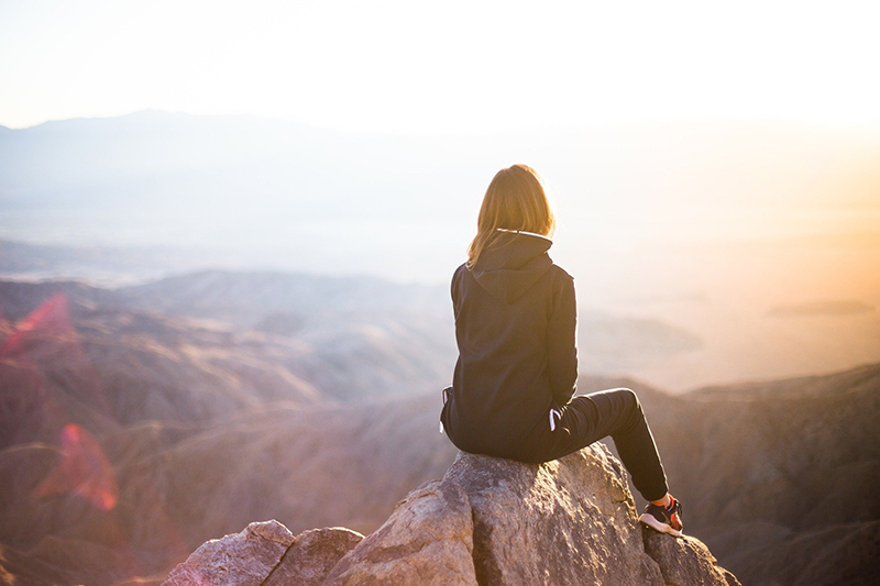 woman siting on a mountain looking out is it weird to travel solo