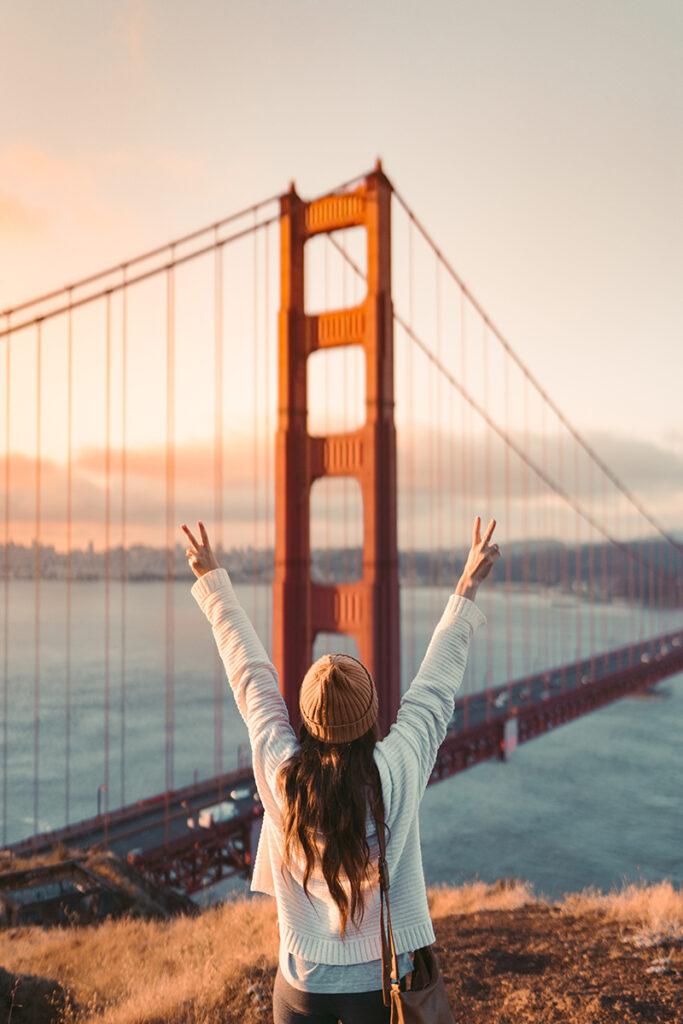 Woman standing at the Golden Gate Bridge in California with her hands in the airi